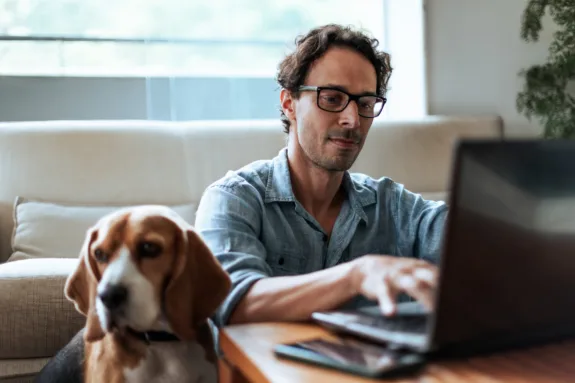 Mid-aged man comfortably working at home sitting on the floor with his dog